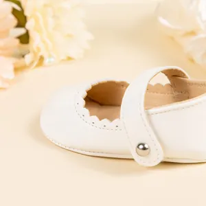 Gros plan sur chaussure Mary Jane blanche bébé avec bords festonnés et boucle argent