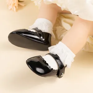 Gros plan de chaussures bébé Mary Jane en cuir verni noir avec bords festonnés et dentelle