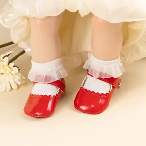 Détail de chaussures bébé en cuir verni rouge avec bords festonnés et bride à boucle