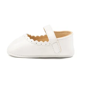 Détail de chaussures bébé en vernis blanc avec bords festonnés et bride velcro