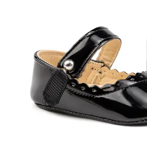 Détail de chaussures bébé en cuir verni noir avec bords festonnés et boucle argentée