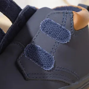 Detail of dark blue children shoes with brown leather collar and velcro stitching