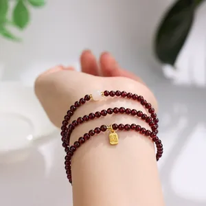 Three-layer garnet bead bracelet with white jade bead and gold Fu charm on wrist