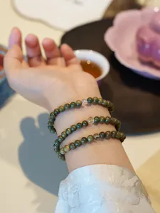 Close-up of green sandalwood bead wrap bracelet with white jade gourds on a wrist