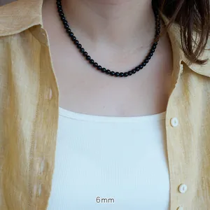 Detailed view of 6mm natural black onyx beaded necklace worn on a yellow linen shirt
