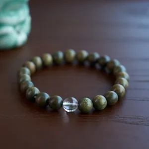 Macro shot of green sandalwood beads with a white jade gourd on a rustic wooden base
