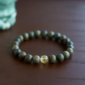Close-up of green sandalwood beads with a yellow gemstone on a dark wooden surface