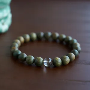 Detail of green sandalwood prayer beads with a clear crystal bead on wood background
