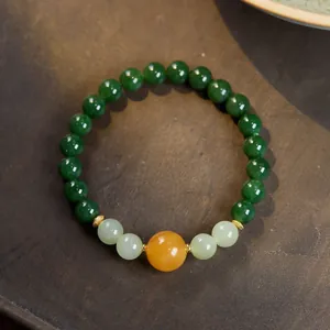 Detail of green jasper and amber beads bracelet with golden floral spacers on wooden tray