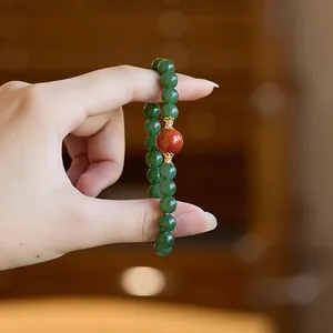 Macro view of jade bracelet with green beads, a red focal bead, and gold flower caps