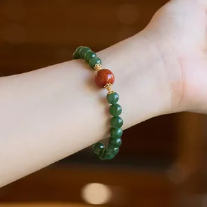 Close-up of a dark green jasper bead bracelet with red agate and gold accents on wrist