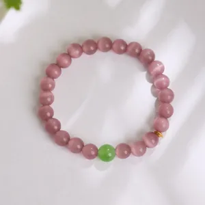 Macro view of pink opal beaded bracelet featuring a green jade bead and gold spacer