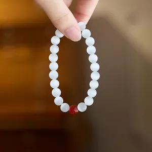 Close-up of beaded opal bracelet with white cat eye stones and one red agate accent