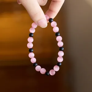 Detail of pink cat-eye and black beaded bracelet with smooth round stones and elastic cord