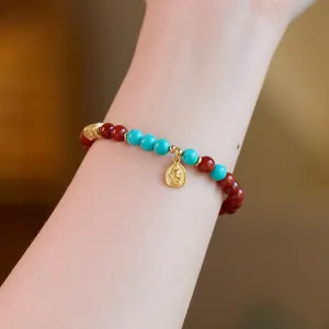 Detail of red agate beaded bracelet with turquoise accents and gold Buddha charm