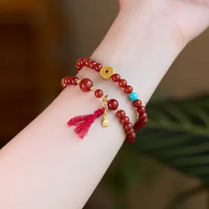 Detail of red agate bead bracelets with gold Fu pendant and tassel on a female wrist