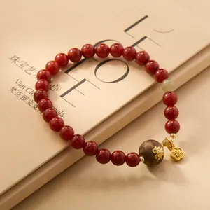 Macro detail of red agate bracelet featuring gold lion bead and lucky flower pendant
