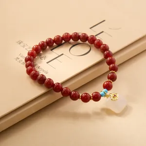Detail of red agate bead bracelet featuring a white jade square charm and gold plum clasp