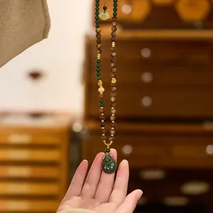 Κοντινό πλάνο του μενταγιόν κολοκύθας από νεφρίτη με ξύλινες χάντρες και πλεκτό κορδόνι