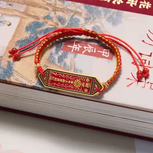 Détail du bracelet en corde rouge tissée avec charme en émail doré et perles
