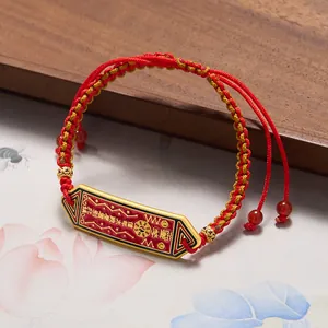 Détail du bracelet tressé rouge et jaune avec amulette dorée de la chance du zodiaque
