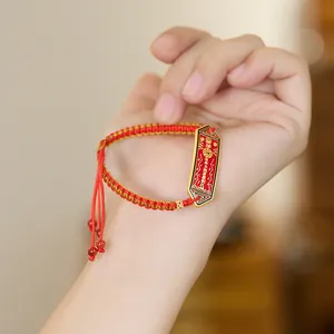 Gros plan d'un bracelet tressé rouge et or avec une breloque en émail et mantra gravé