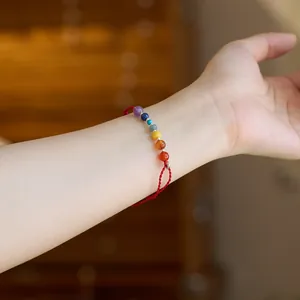 Nahaufnahme von rotem geflochtenem Armband mit sieben bunten Chakra-Perlen am Handgelenk