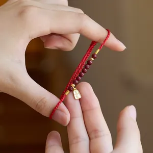Detail eines roten geflochtenen Glücksarmbands mit Perlen und goldenem Anhänger