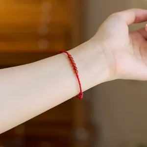 Detail eines geflochtenen roten Armbands mit sechs polierten Perlen an einem Handgelenk