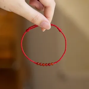 Detail eines roten geflochtenen Glücksarmbands mit sechs durchscheinenden Karneolperlen