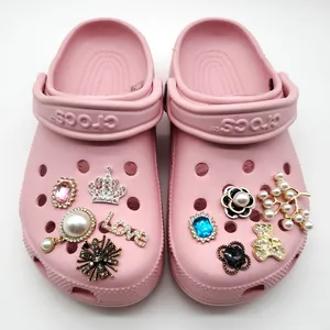 Pink garden clogs adorned with crystal gems, pearls, and gold charms on white background