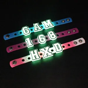 Nahaufnahme von drei leuchtenden LED-Silikonarmbändern mit Buchstaben und Metallknöpfen