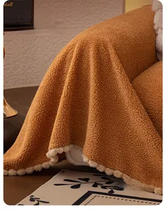 Détail d'une jetée de canapé en polaire marron avec pompons décoratifs sur le bord