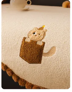 Detail of plush teddy fleece sofa cover with cute cat embroidery and pom-pom fringes