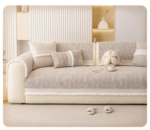 Close-up of beige chenille sofa cover with white lace edges and decorative pom-pom fringe