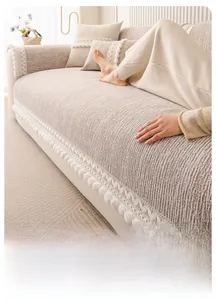 Detail of beige sofa cover with striped texture, lace border and white pom-poms
