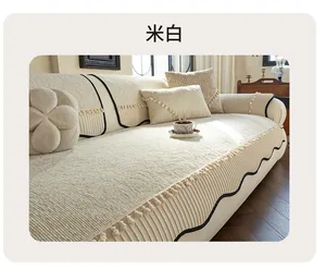 Detailed texture of off-white chenille sofa cover with wavy edges and pom-pom tassels