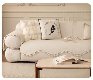 Detail of cream chenille sofa cushion with wavy edges and decorative white pom-poms