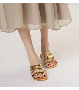 Detail of gold metallic flat sandals with triple adjustable buckle straps on a model