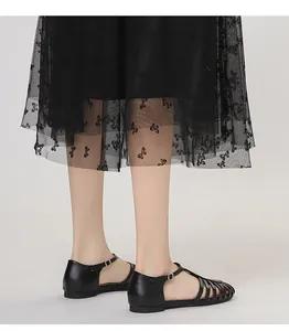 Vista en pies de sandalias romanas negras caladas con una falda de tul con mariposas