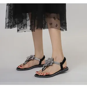 Close-up of sparkling rhinestone flower on black flat sandals with T-strap design