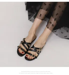 Detail of black flat sandals with thin cross straps and decorative gold square buckles