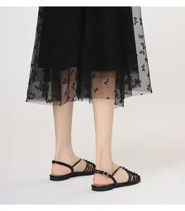 Detalle de sandalias planas negras de tiras finas con hebilla en una modelo con falda