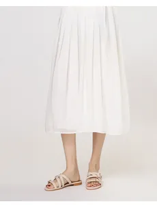 Detail of beige multi-strap flat sandals with gold buckles worn with a pleated skirt