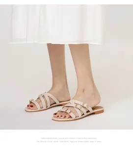 Detail of cream multi-strap flat sandals with gold buckles worn with a white dress