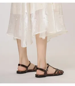 Detail von bronzefarbenen gewebten flachen Sandalen mit verstellbarem Knöchelriemen