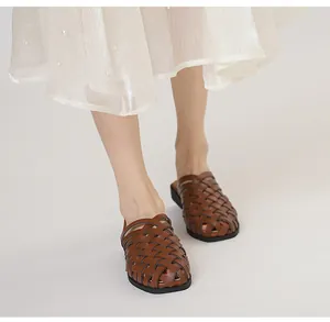 Detalle de mules de cuero marrón trenzado con diseño calado en el pie de la modelo