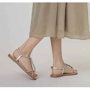 Close-up of sparkling rhinestone bow detail on silver T-strap flat sandals for women