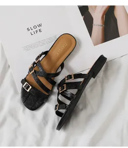 Detail view of black multi-strap flat sandals with faux crocodile texture and gold buckles