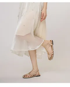 Detail von beigen geflochtenen flachen Sandalen mit Riemen und elegantem Knöchelverschluss